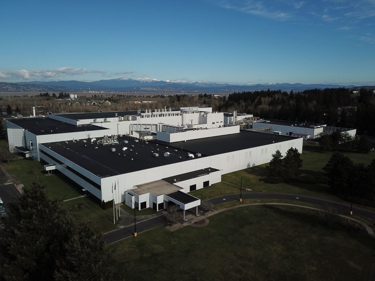 A low-slung white industrial building with snow-capped Cascade foothills in the backround.